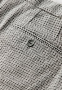 Tissu à carreaux gris avec une finition texturée, comprenant un petit bouton noir et un détail de poche.