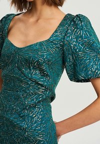 Vestido verde azulado con escote cuadrado, mangas abullonadas y un patrón texturizado con acentos metálicos en tonos dorado y plateado.