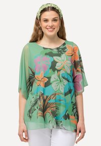 Gennemsigtig, grøn bluse med blomsterprint i store orange, pink og blå blomster, med løse korte ærmer og rund halsudskæring.