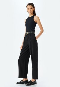 Top sin mangas de color negro con canalé combinado con pantalones negros de cintura alta. El conjunto incluye un cinturón elegante y mocasines negros brillantes. Textura suave.