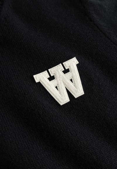 Tela de punto negra con una destacada letra "W" bordada en blanco como detalle, con una textura suave y una vista en primer plano.
