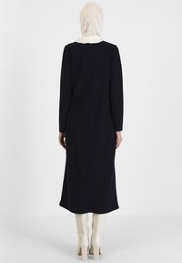 Navy long dress with long sleeves, smooth texture, rear zipper details, paired with knee-high cream boots. Simple, elegant silhouette.