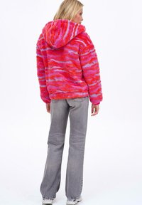 Różowo-fioletowy kominowy polarowy sweter z teksturowaną, puszystą powierzchnią, z kapturem i elastycznym pasem. Połączony z szarymi dzwonami dżinsowymi.