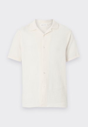 Camisa blanca de manga corta con botones, tejido texturizado y cuello pequeño y puntiagudo, mostrada sobre un fondo claro y simple.