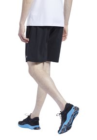 Sorte atletiske shorts laget av lett stoff, med en løs passform. Kombinert med svarte sko med blå såler og teksturerte accenter.