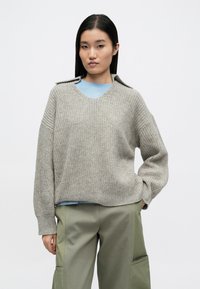 Helehall kootud kampsun V-kaelusega, millel on tekstuuriga muster ja õlale accentid, kombineeritud oliivroheliste lahtiste pükstega.