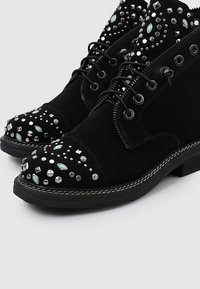 Botines de ante negros con acentos de tachuelas, rhinestones y elementos turquesa. Punta redondeada y suela texturizada. Diseño con cordones.