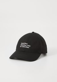 Fekete baseball sapka fehér hímzett szöveggel, amely David Sims, Kate Moss 1993 és Calvin Klein nevére utal az elülső panelen.