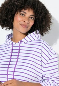 Sudadera con capucha blanca con rayas moradas, con capucha ajustable mediante cordón y corte holgado. Textura suave, diseño informal y mangas cortas.