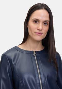 Marineblaue Lederjacke mit rundem Kragen, Reißverschluss vorne und genähten Akzenten. Glatte Textur und taillierte Passform.