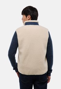 Veste en polaire avec un dos crème et des manches texturées bleu marine. Col haut, poches avant et tissu doux pour chaleur et confort.