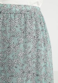 Lichtgroene bloemenrok met een geplooide elastische tailleband. Voorzien van zwart-witte, gedetailleerde bloemenpatronen op een gestructureerde stof.