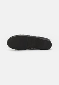 Semelle de chaussure noire à enfiler avec une texture lisse, construction en caoutchouc et accents cloutés sur le côté. Design plat pour un usage décontracté.