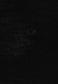Tessuto nero con una trama texturizzata presenta un sottile logo "CK" in rilievo. Il materiale appare resistente e liscio.