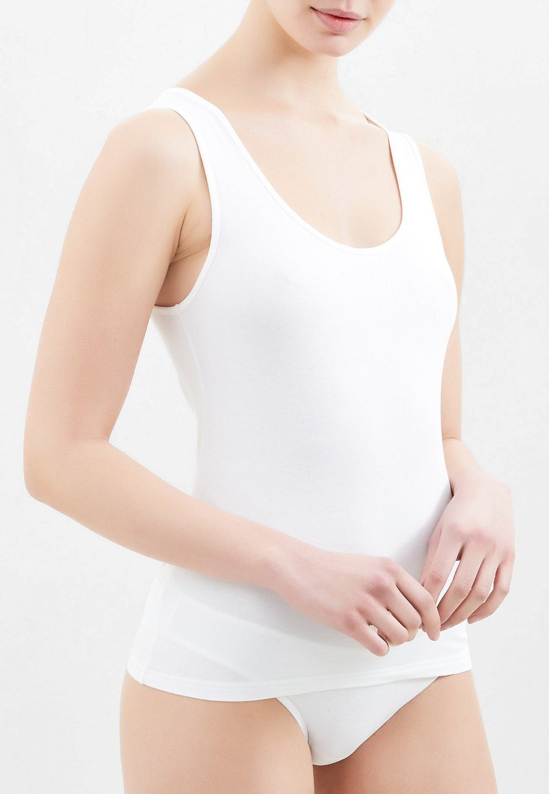 Top bianco senza maniche realizzato in tessuto liscio, con scollatura rotonda e spalline larghe. Il corpo è aderente e si estende fino all'anca.