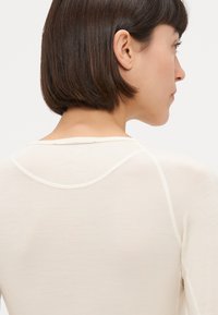 Haut beige clair avec un col rond, texture douce et design ajusté. Présente une couture contrastante le long des coutures.