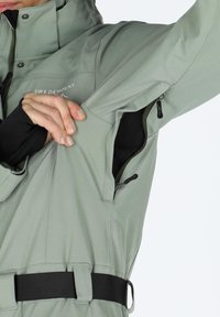 Light green zip-up jacket with a fitted design, side pocket, and adjustable black belt detail. Features smooth texture and breathable lining.