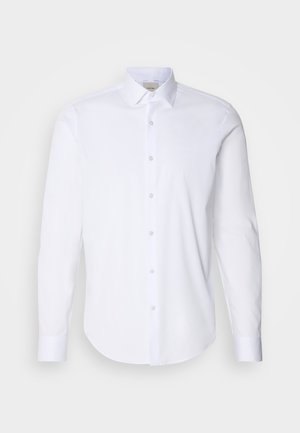 Camisa blanca de manga larga hecha de una suave tela de algodón. Presenta un cuello puntiagudo, un cierre frontal con botones y un dobladillo redondeado. Sin patrones ni acentos.