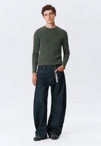 Grønn langermet t-skjorte kombinert med oversized mørkeblå denimjeans. Jeansene har en lommechain i rutete mønster. Uformell fottøy.