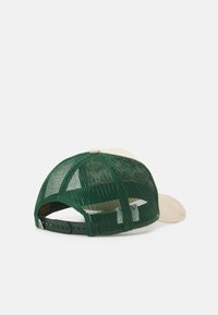 Casquette trucker verte en maille avec un visière en velours côtelé beige, dotée d'une fermeture à pression en plastique et d'un patch logo près de la base à l'arrière.