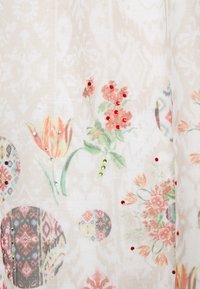 Tessuto beige con stampe floreali e motivi geometrici circolari, decorato con piccole strass rossi, verdi e argentati.