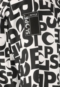 Mustavalkoinen takki, jossa on suuria lohkovirheitä sileällä kankaalla. Takissa on suorakulmainen etiketti, jossa lukee "SLOPE STYLE."