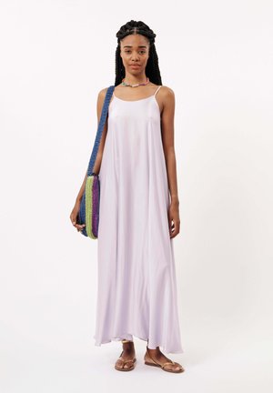 Robe maxi lavande clair avec bretelles spaghetti, tissu fluide, texture douce. Accessoirisée avec un sac tissé multicolore et des sandales plates.