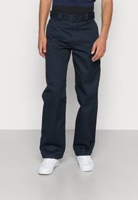 Navy blue trousers with a smooth texture, straight-leg design, and a belt. Paired with white sneakers on a light gray floor.
