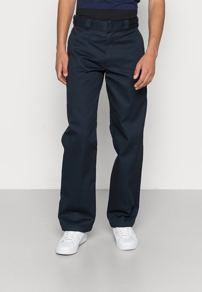 Navy blue trousers with a smooth texture, straight-leg design, and a belt. Paired with white sneakers on a light gray floor.