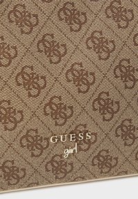 Brunt tekstureret materiale med et diamantmønster og sammenflettede design. "GUESS girl" logo i guld nederst.