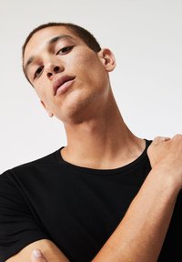 T-shirt nero a maniche corte con collo rotondo, texture liscia, design aderente e dettagli di cucitura minimi, indossato da una persona dalle spalle in su.