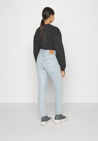 Svart långärmad skjorta med texten "Levi's California" på baksidan, ihop med ljusblå högmidjade jeans och grå höga sneakers.