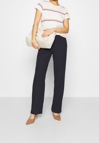 Stribet t-shirt i hvid, rød og blå, parret med marineblå brede bukser. Holder en struktureret beige taske; iført brune spidse hæle.