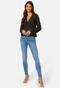 Dunkel gestreiftes langärmeliges Oberteil mit verdrehtem Vorderteil, kombiniert mit hellblauen Skinny Jeans und nudefarbenen High Heels.