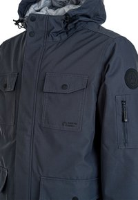 Mørk grå jakke med aftagelig hætte, flere lommer, trykknaplukninger og et logo-patch. Glat, vandafvisende stof med en mat finish.