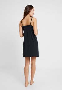 Svart ärmlös klänning med avslappnad passform, tillverkad av mjukt tyg, med justerbara axelband och knälång fåll.