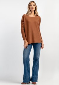 Brązowy sweter dzianinowy z szerokim dekoltem, długimi rękawami i luźnym krojem, w połączeniu z dżinsami w kolorze niebieskim z rozszerzanymi nogawkami i haftowanym wykończeniem.