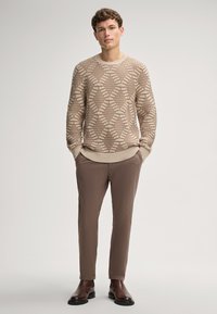 Maglione beige a motivo geometrico, abbinato a pantaloni slim-fit marroni e stivaletti alla caviglia marroni scuri. Texture liscia in tutto il capo.