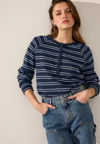 Marine gestreiftes Langarmoberteil mit Rundhalsausschnitt, Knopfleiste auf der Vorderseite und gerippten Bündchen, kombiniert mit hellblauen baggy Jeans.