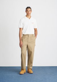 Witte poloshirt met logo, beige broek en gele laarzen. Glad materiaal, relaxte pasvorm, met een knoopsluiting en zijzakken.