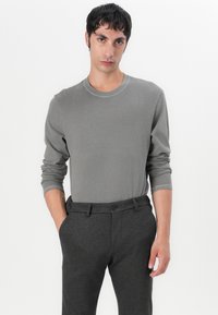Graues Langarmshirt mit geripptem Rundhalsausschnitt, kombiniert mit dunkelgrauen Hosen mit Knopfverschluss und Gürtelschlaufen. Glatte Textur.