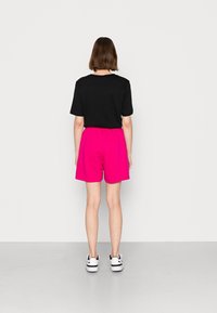 Black short-sleeve shirt paired with pink shorts. The shorts have an elastic waistband. The outfit is completed with white sneakers.