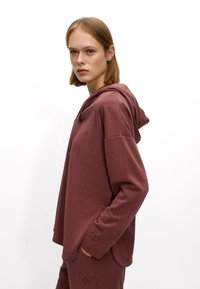 Maroon hoodie made of soft fabric, featuring a relaxed fit, hood, and subtle embroidered accents on the cuffs. Smooth texture, minimal design.
