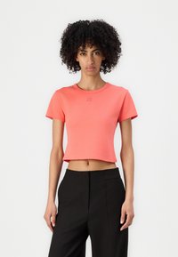 Korálový crop top s krátkymi rukávmi a okrúhlym výstrihom, vyrobený z jemného materiálu. Obsahuje vyšívané logo na hrudi.