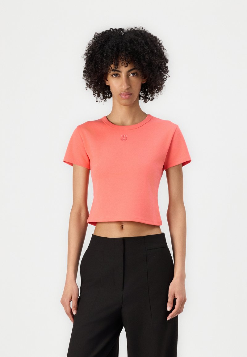 Korálový crop top s krátkymi rukávmi a okrúhlym výstrihom, vyrobený z jemného materiálu. Obsahuje vyšívané logo na hrudi.