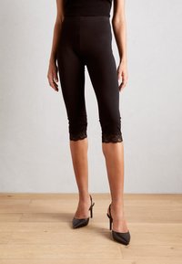 Leggings capri noirs avec dentelle sur l'ourlet. Tissu lisse et extensible avec une coupe slim, dotés d'une taille élastique.