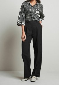 Black high-waisted trousers paired with a black and white patterned button-up shirt featuring various geometric designs and a chest pocket.