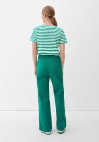 Zelené široké kalhoty z bavlny s vysokým pasem, doplněné kratším tričkem se zeleno-bílými pruhy a krátkým rukávem.