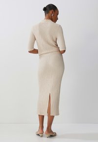 Beige Strick-Koordinatenset mit einem taillierten Oberteil und einem Midirock mit seitlichem Schlitz, strukturierter Stoff und kurzen Ärmeln. Minimalistisches Design.