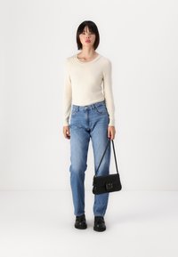 Jersey crema de manga larga con escote decorativo, jeans de cintura alta azul claro, bolso negro con cierre de metal y zapatos negros.